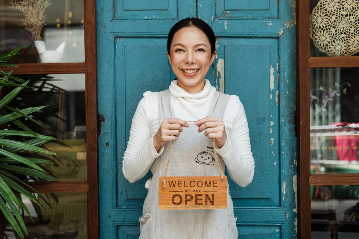 Smiling shop owner holding a Welcome, we're open sign